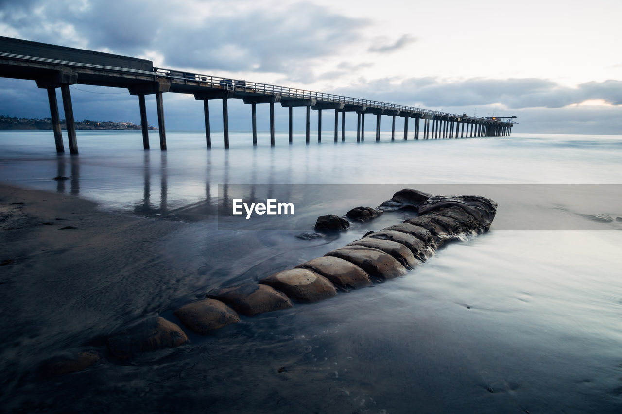 Pier on sea against cloudy sky during sunset