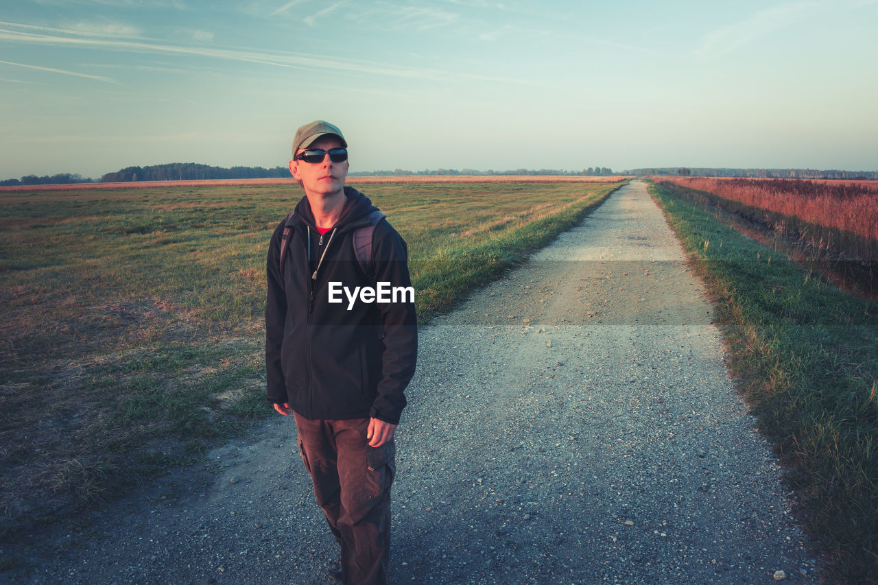 A man in sunglasses with a backpack goes the gravel road, autumn view