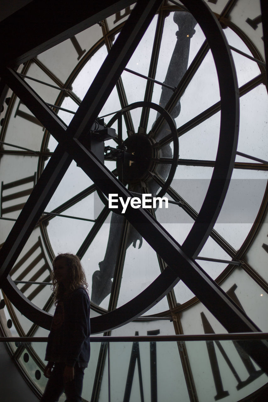 REAR VIEW OF MAN STANDING AGAINST CLOCK