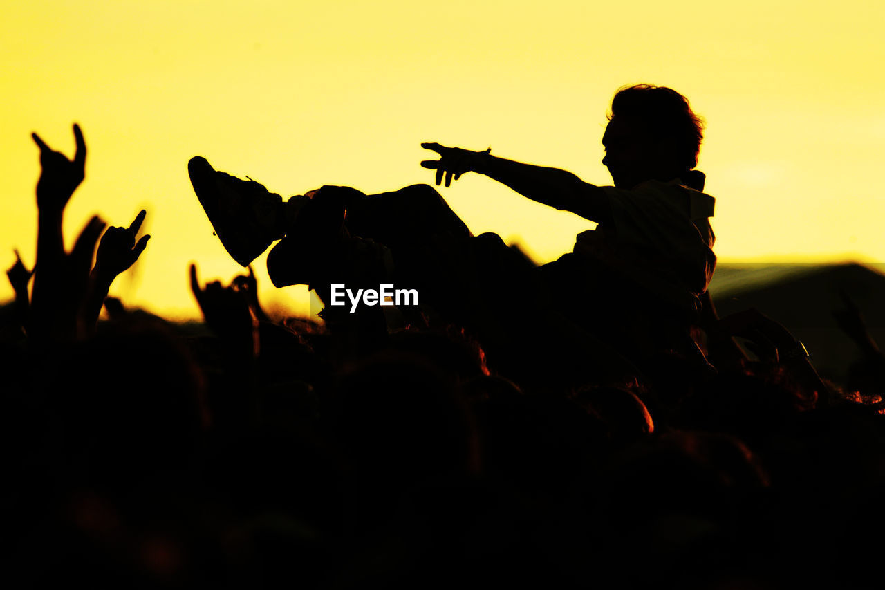 Close-up of silhouette people in concert against sky during sunset