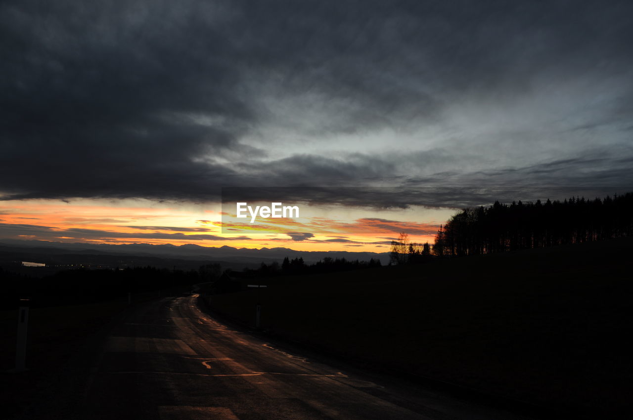 Empty road by field against cloudy sky during sunset