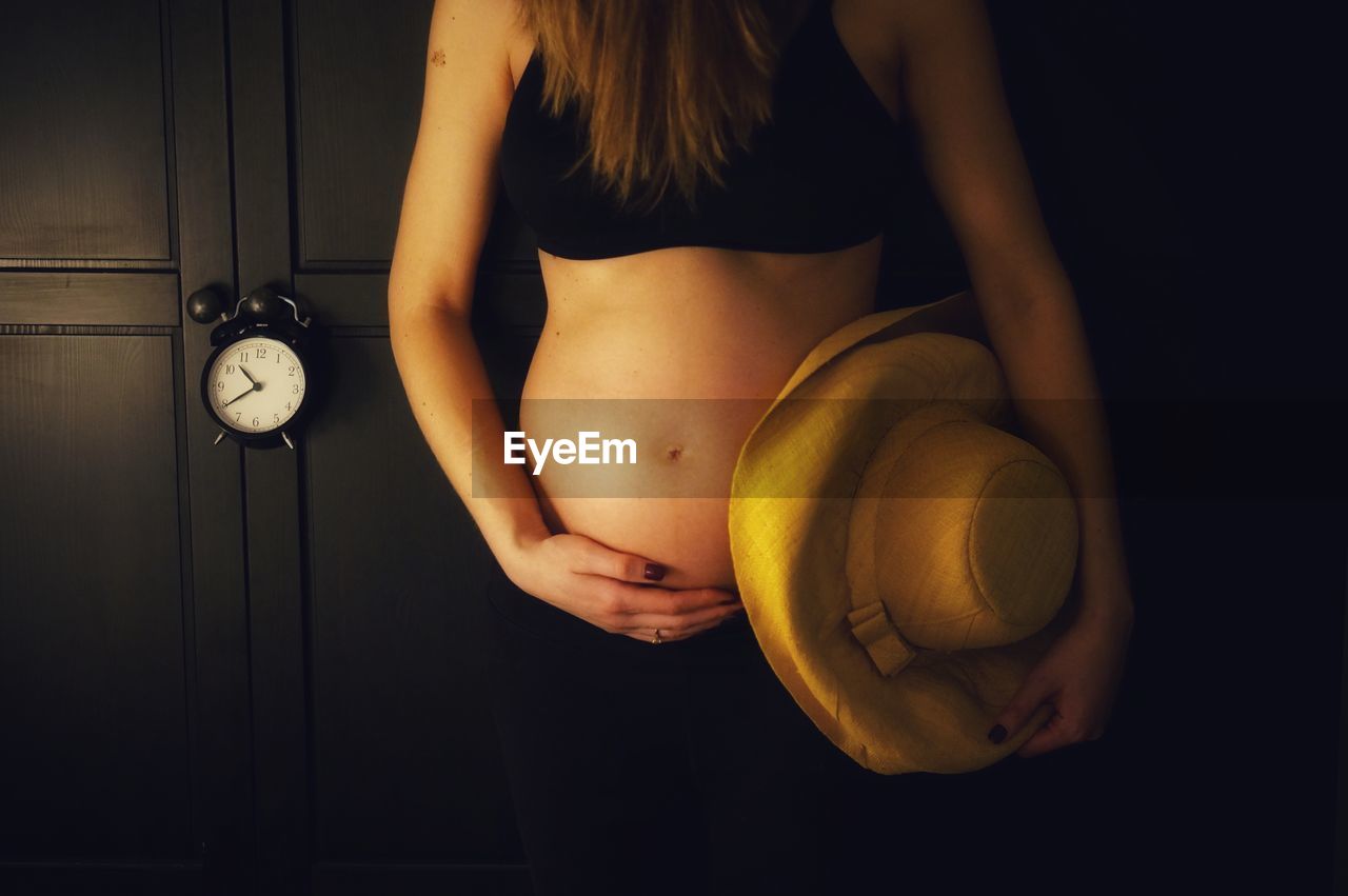 MIDSECTION OF WOMAN STANDING AGAINST BLACK BACKGROUND IN DARK