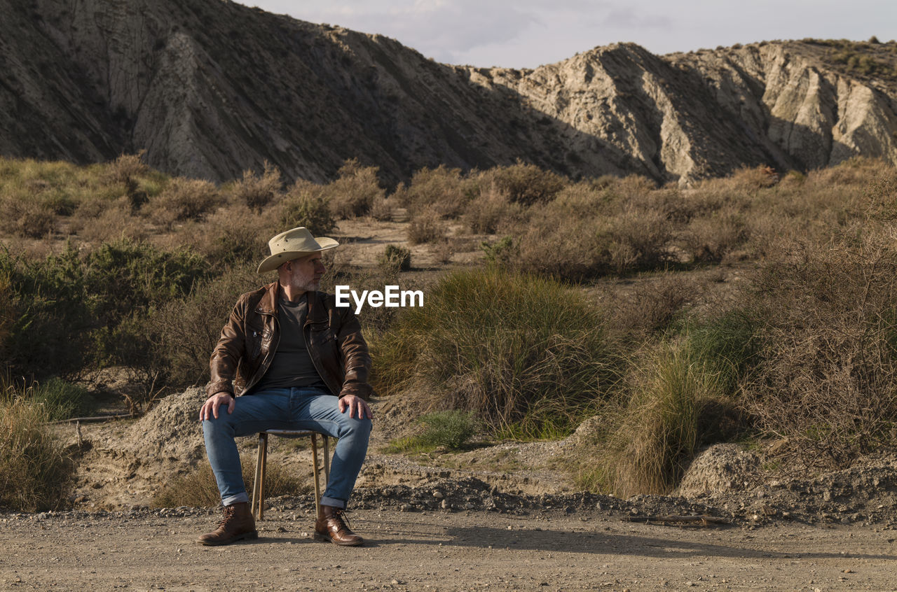 Adult man in cowboy hat sitting on abandoned chair in desert, almeria, spain