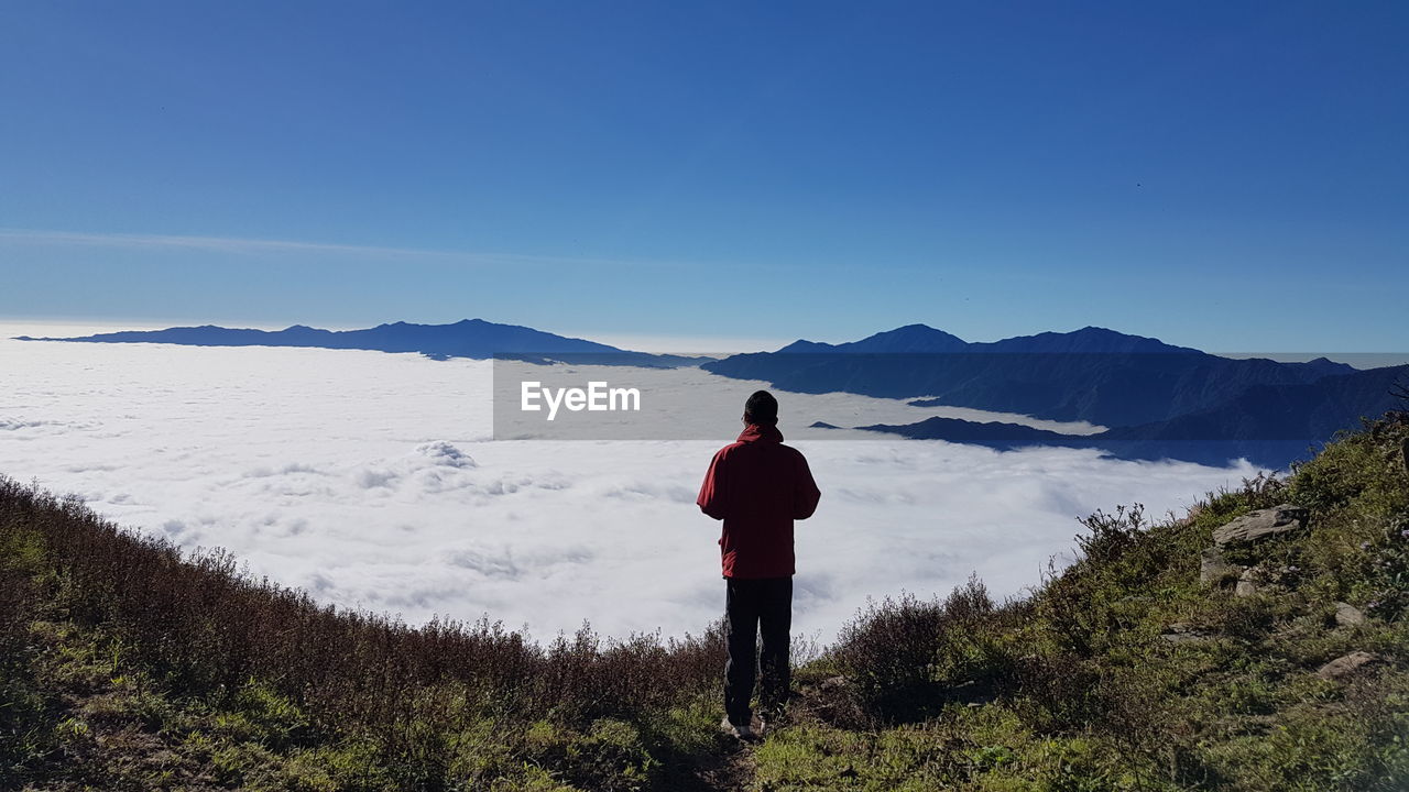 Full length rear view of hiker walking on mountain by cloudscape against sky