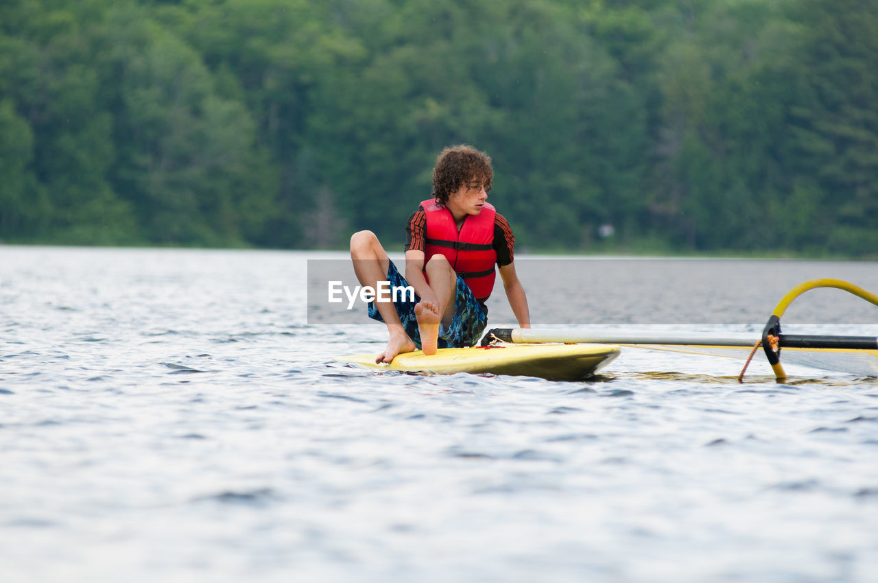 Teenage boy sitting on paddleboard in river