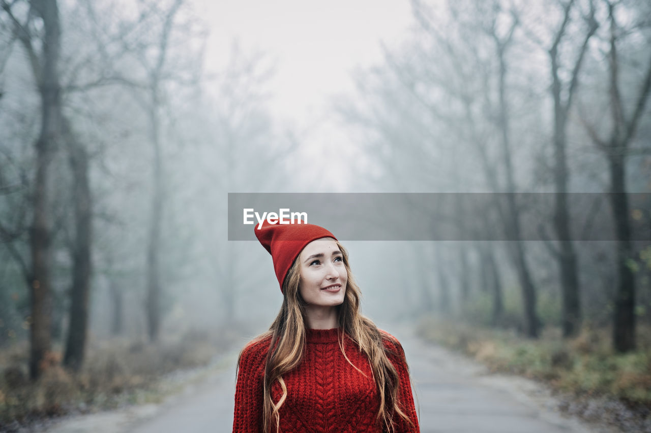 Woman in red hat and sweater walking on foggy mystical morning forest.