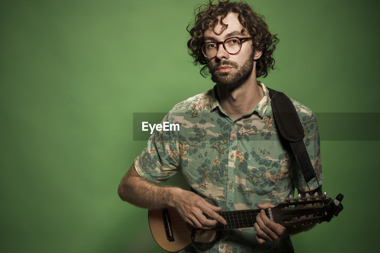 Portrait of young man playing ukulele on green background