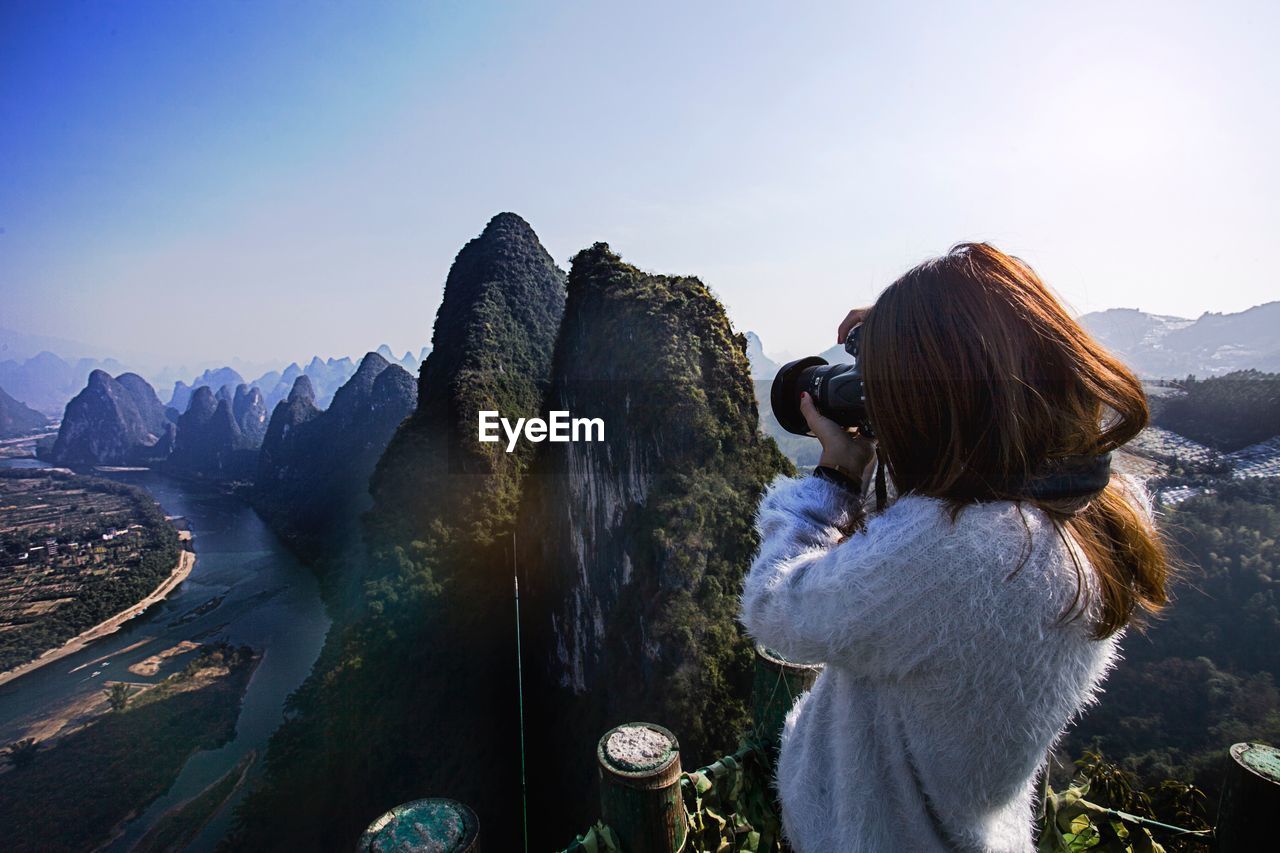 Woman photographing mountains against sky