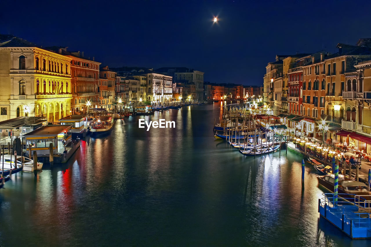 Boats moored on illuminated city at night