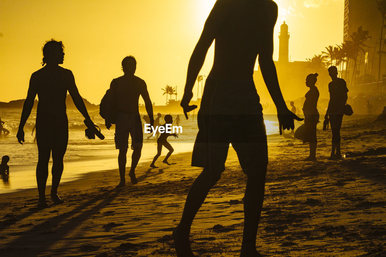 Silhouette people enjoying on beach against sky during sunset