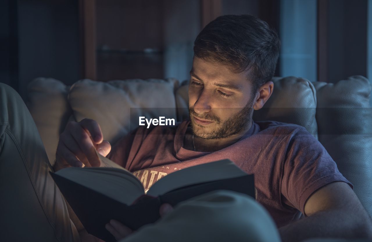 Close-up of man reading book while sitting on sofa at home