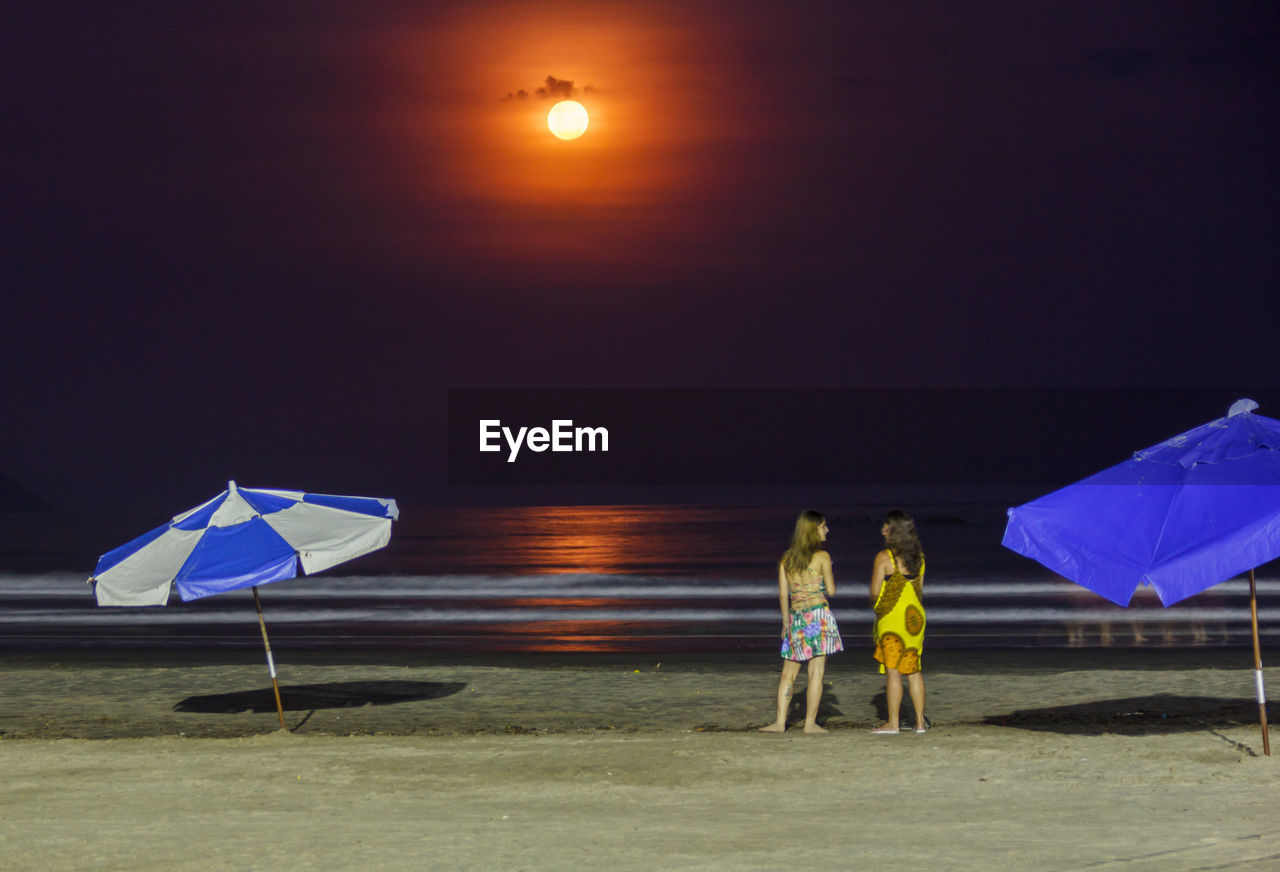 Female friends standing at beach during night