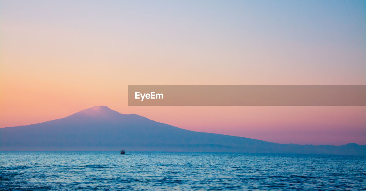 Scenic view of sea by mount etna against sky during sunset