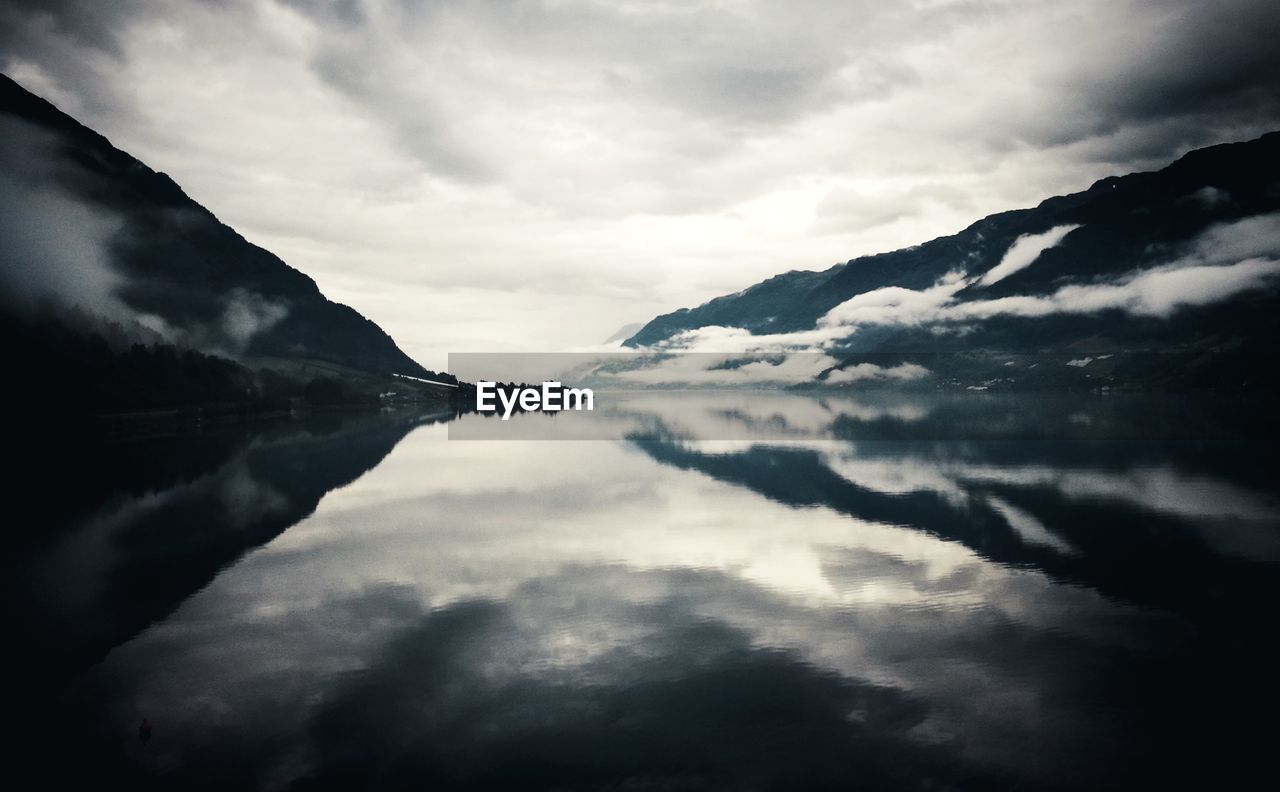 Reflection of clouds in river amidst mountains at dusk