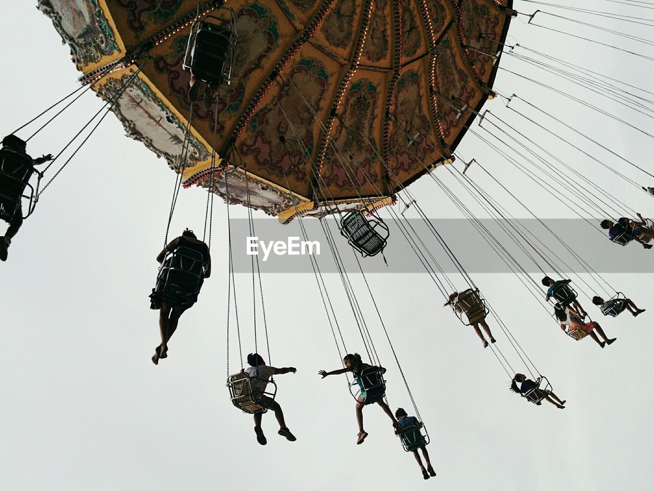 Low angle view of people sitting in carousel against sky