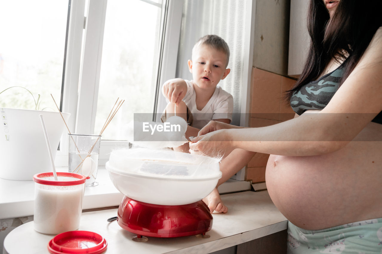 Midsection of pregnant mother and son making cotton candies at home