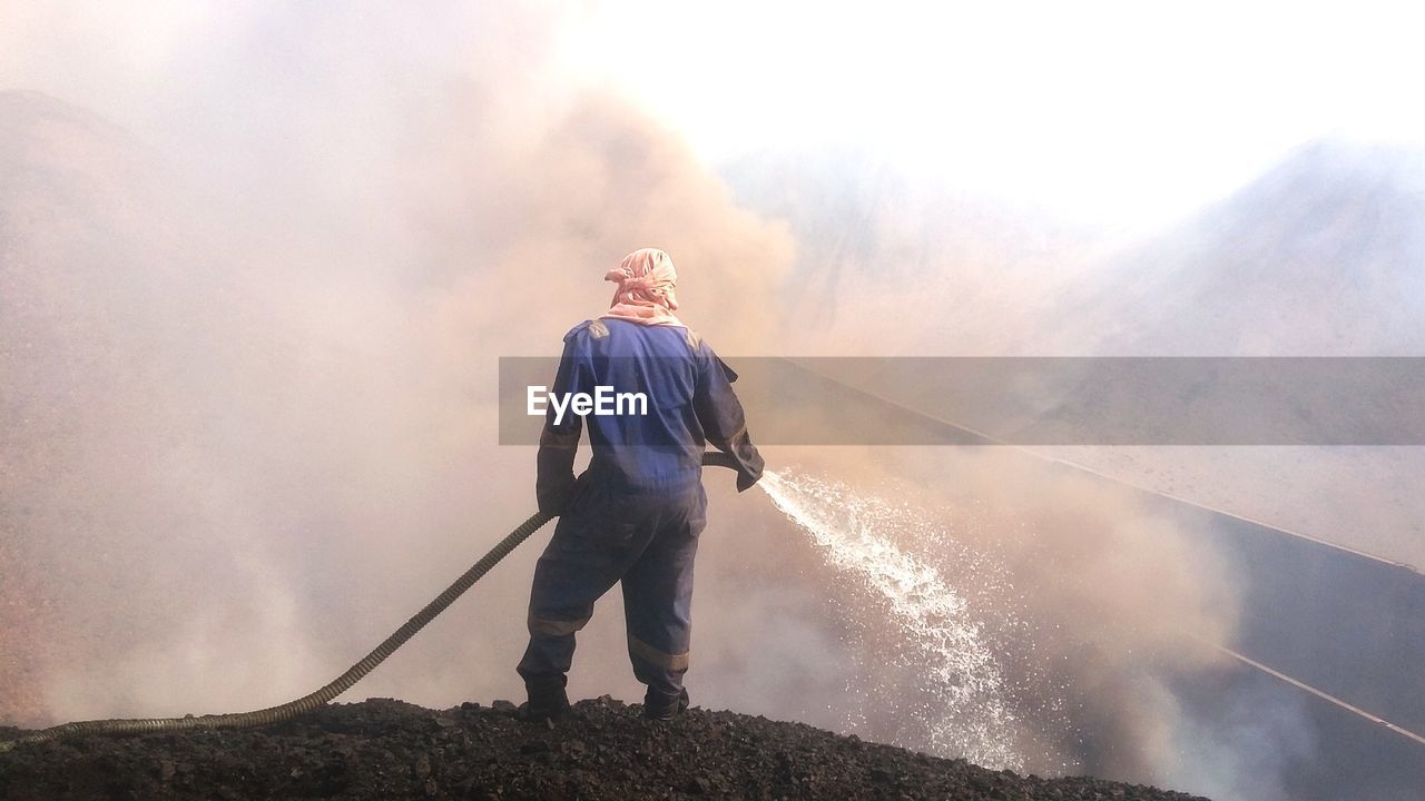 Rear view of a man standing against a burnt coal try to extinguishing it