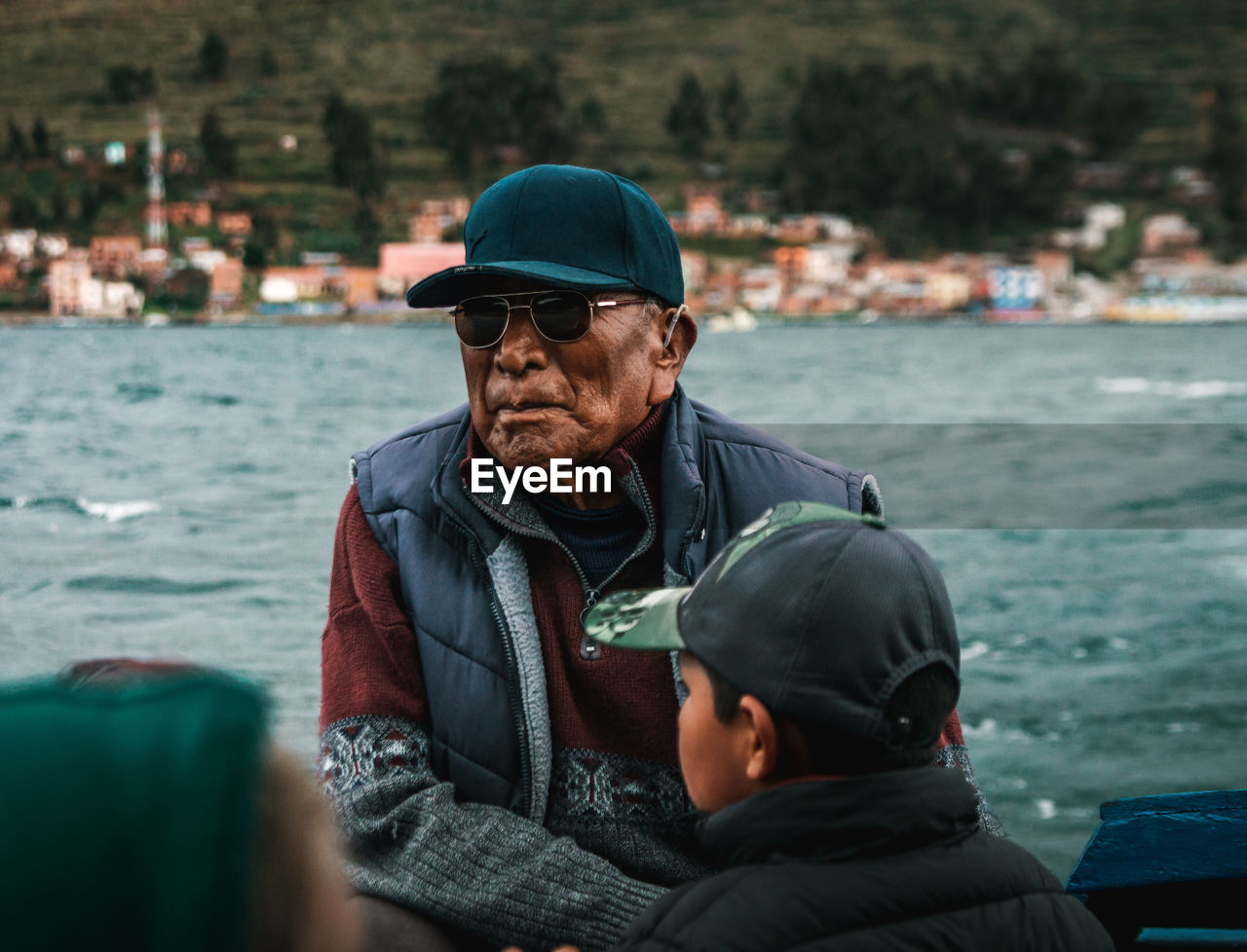 MAN LOOKING AT CAMERA WHILE SITTING ON SEA