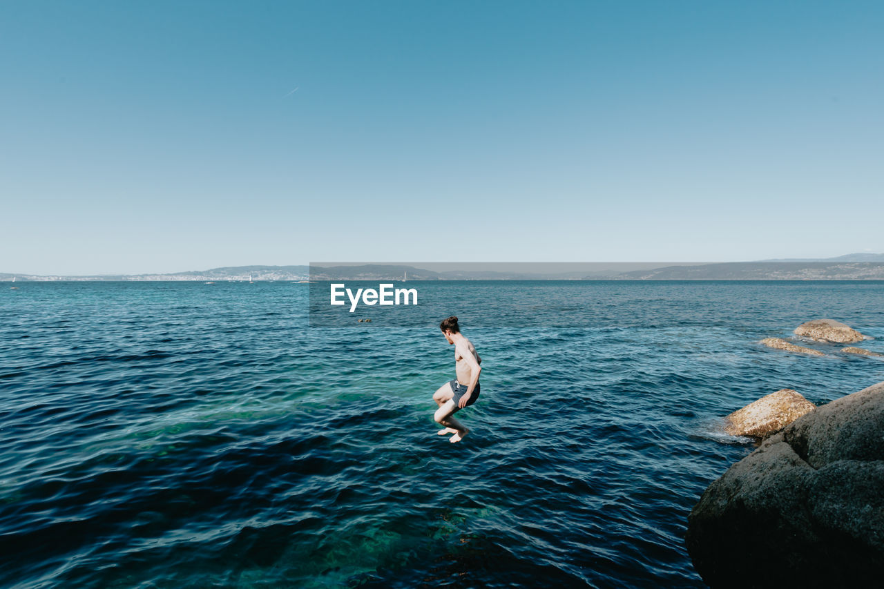 rear view of woman in sea against clear blue sky