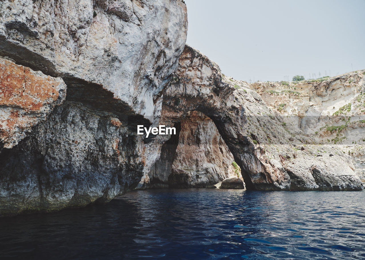 Rock formations in sea against clear sky at the blue grotto on malta