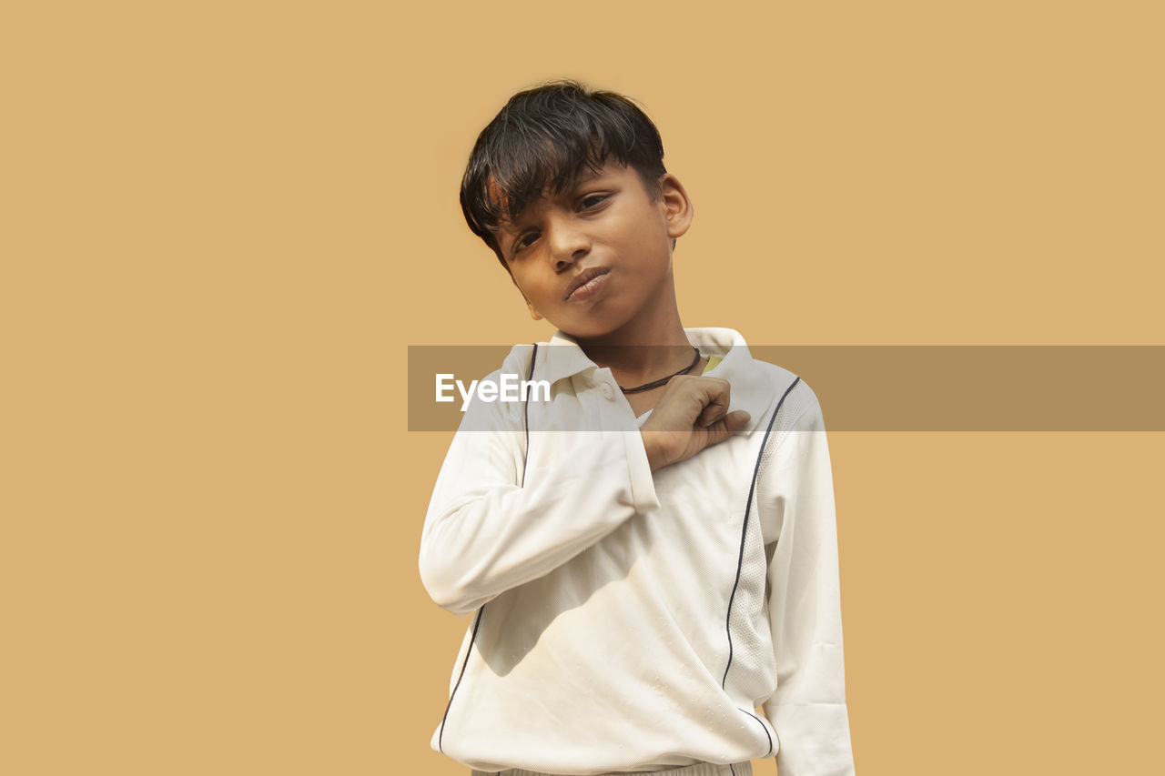 PORTRAIT OF BOY STANDING AGAINST ORANGE BACKGROUND