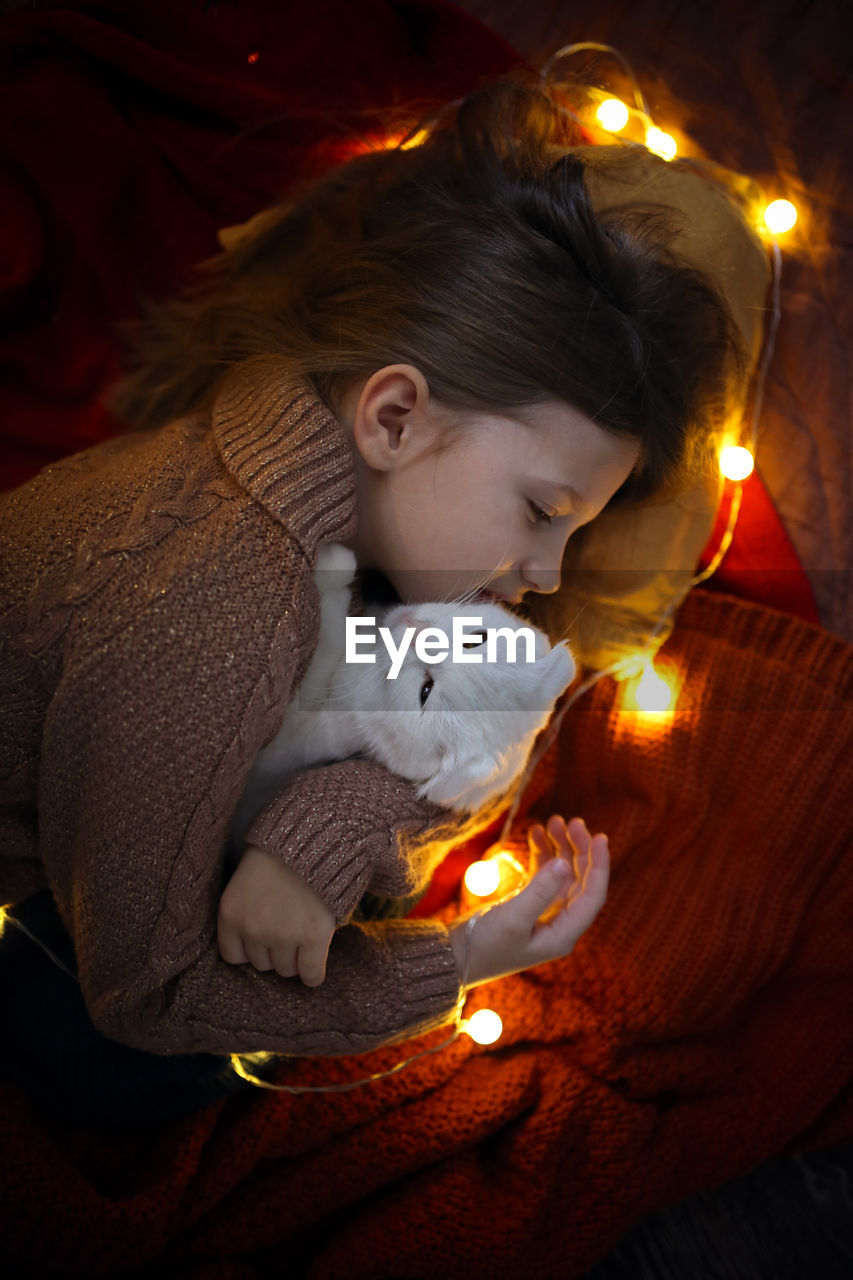 Girl child sleeps in an embrace with a cat blanket and a garland, a cozy childhood and home. 