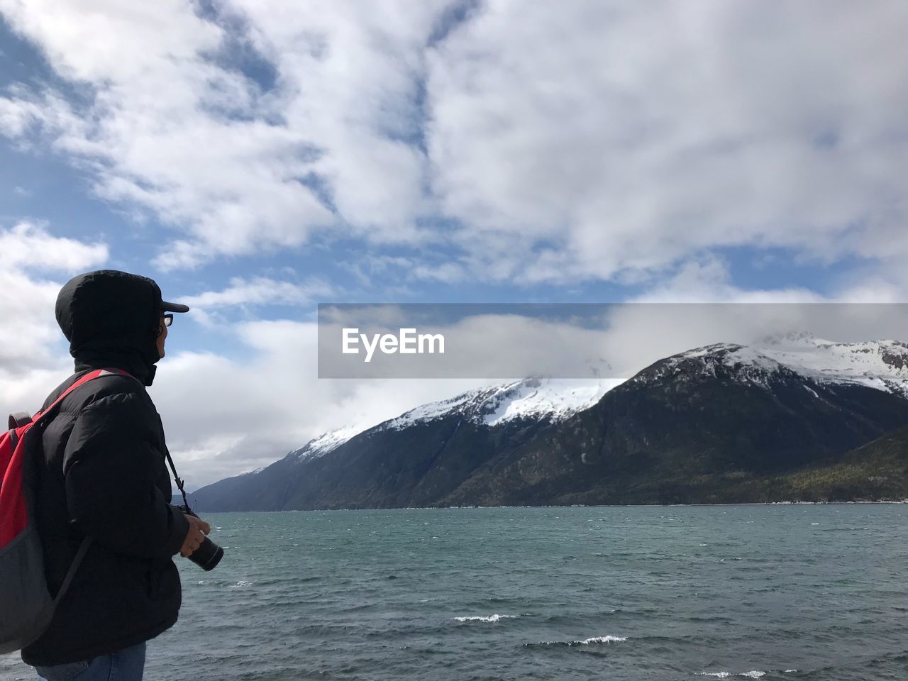 Man looking at snowcapped mountain while standing in sea against sky
