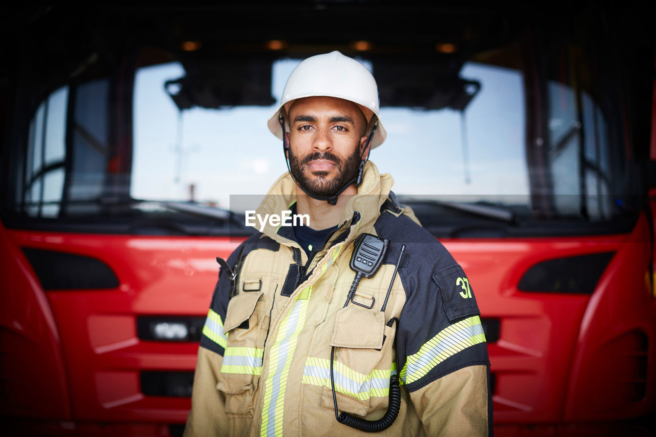 Portrait of confident firefighter standing in front of fire engine at fire station