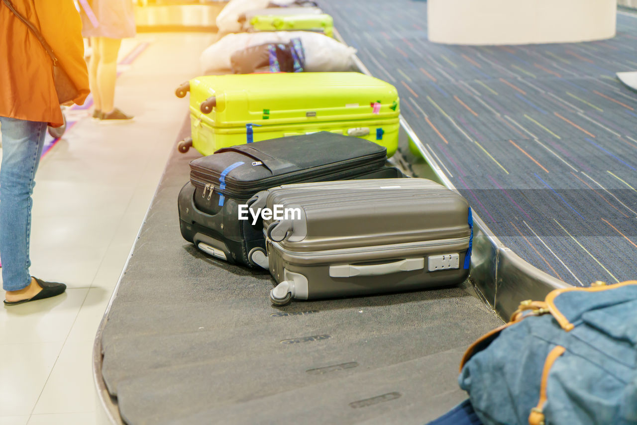 Low section of women standing by suitcases on conveyor belt at airport