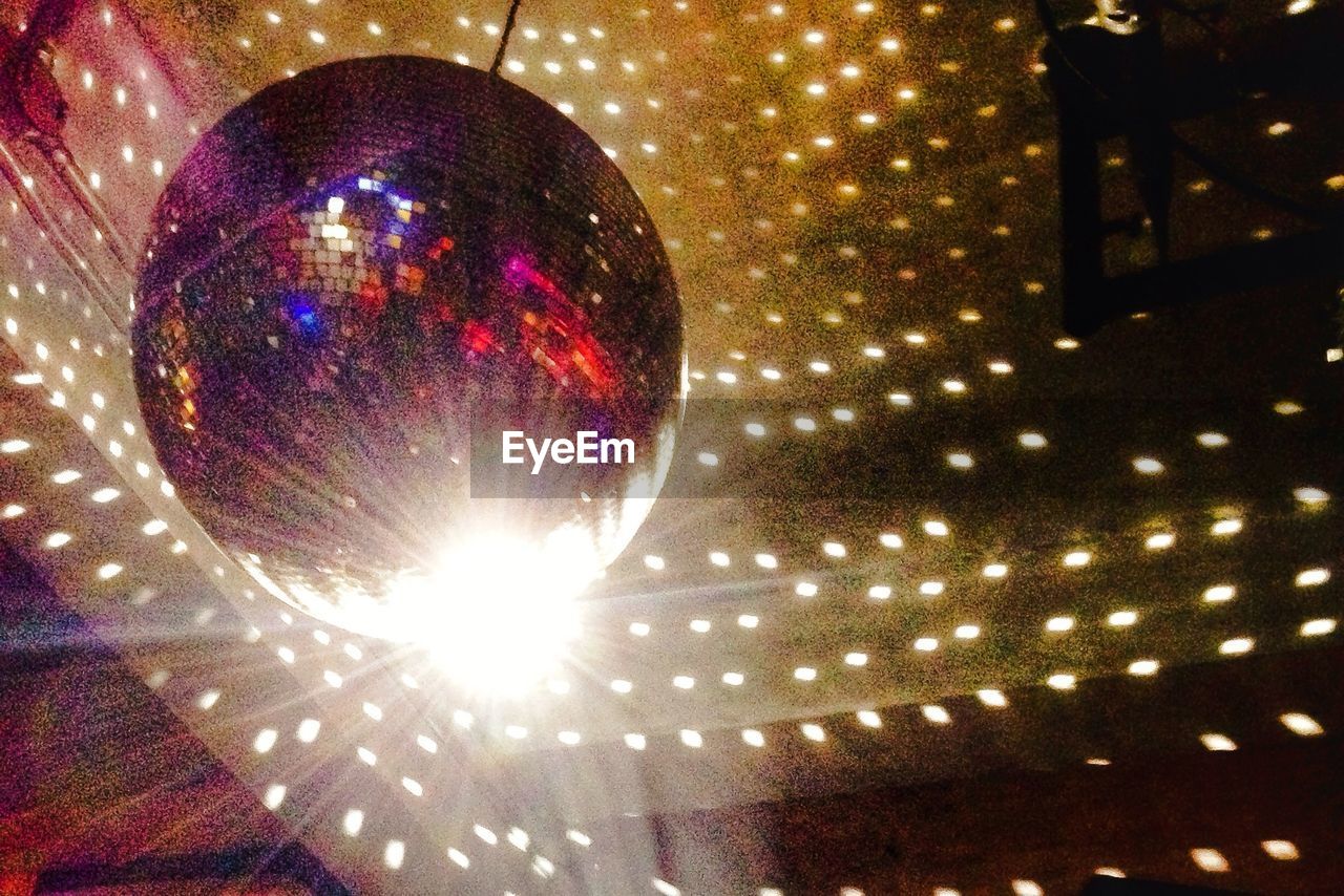 Low angle view of illuminated disco ball hanging on ceiling