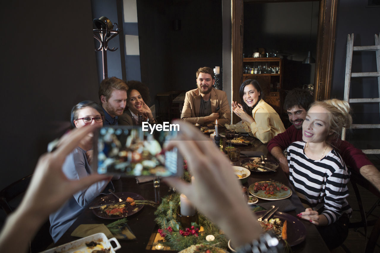 Cropped image of woman photographing happy friends while enjoying meal