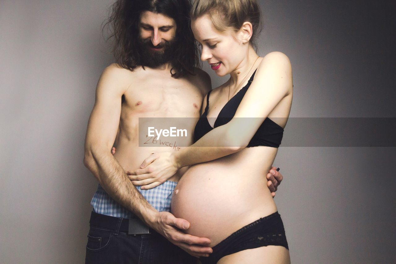 Shirtless with pregnant woman standing against gray background