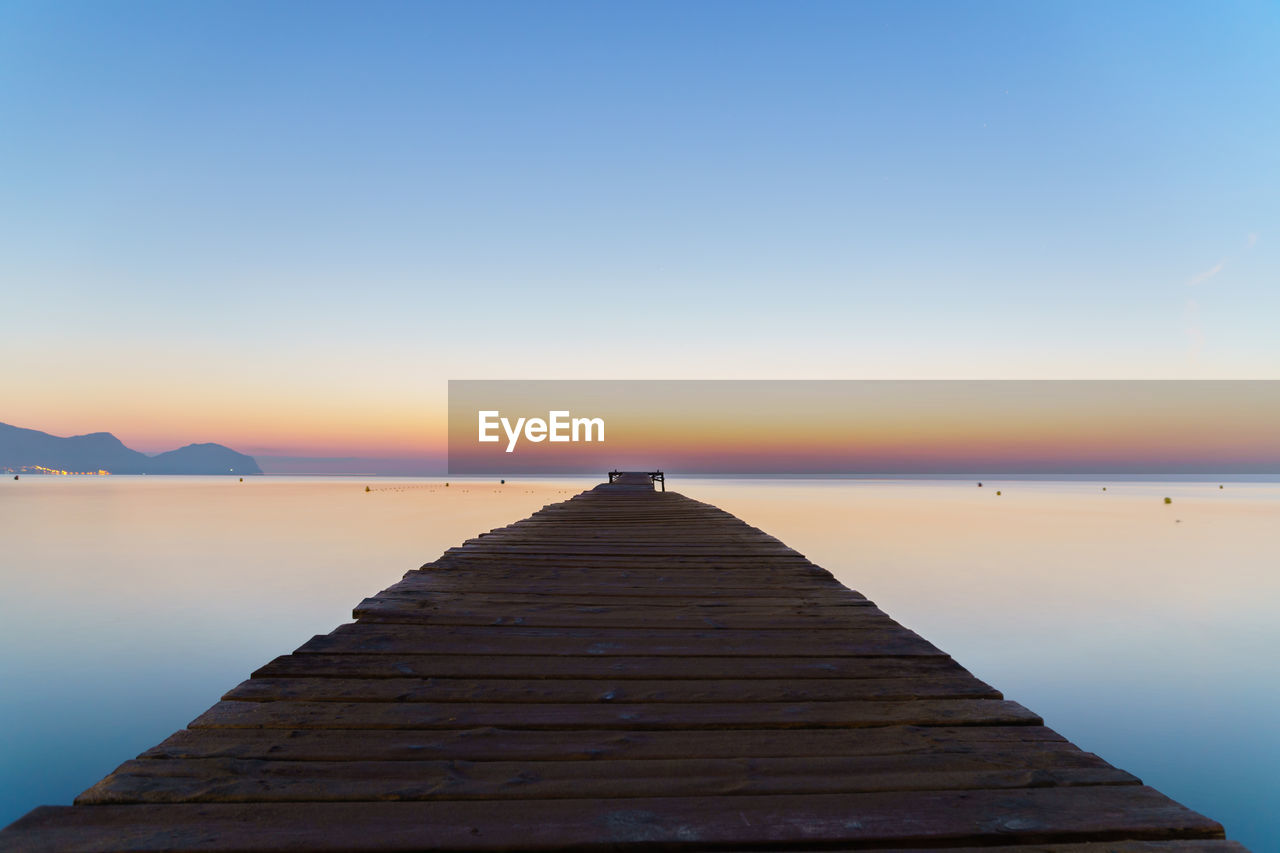 Pier over lake against sky during sunset