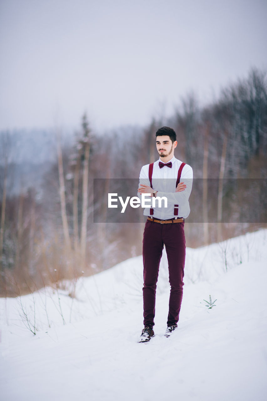 PORTRAIT OF YOUNG MAN STANDING ON SNOWY FIELD