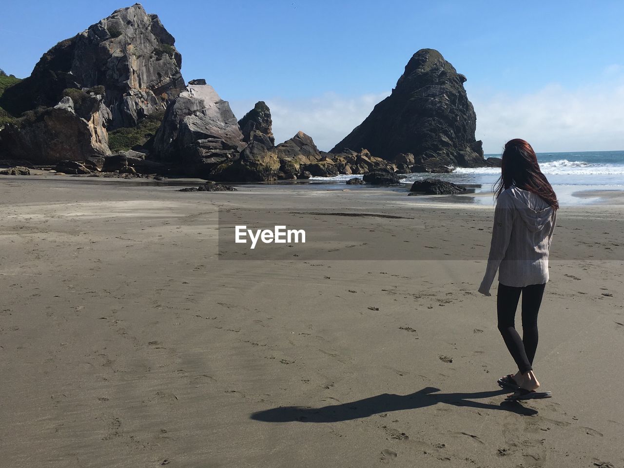 Rear view of woman walking on beach with rocks in the distance