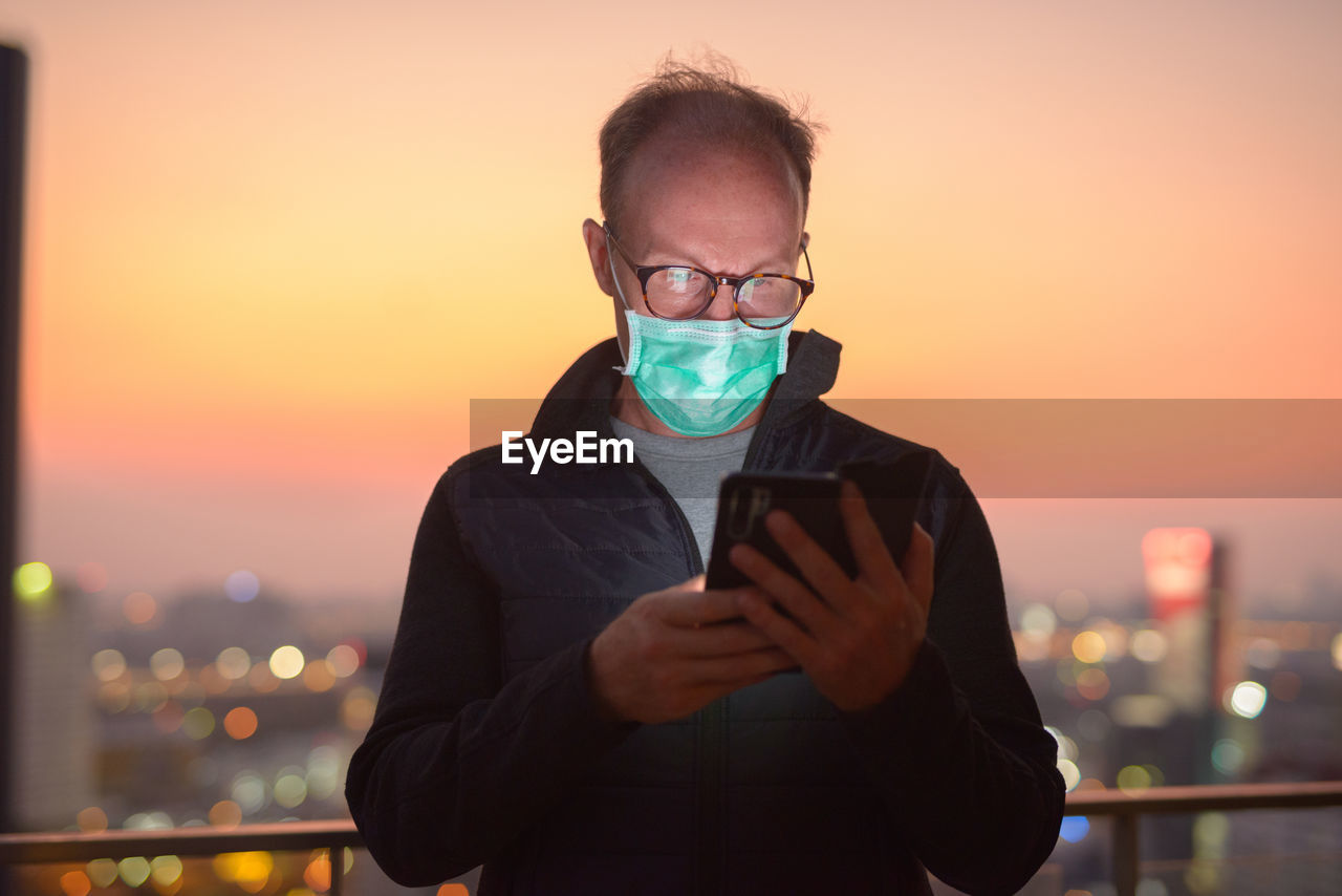 PORTRAIT OF MAN USING SMART PHONE AGAINST SUNSET SKY