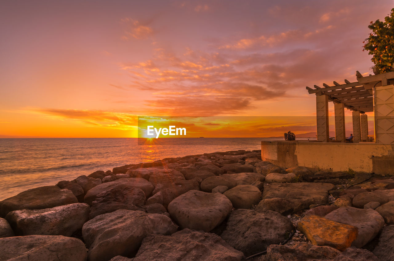 sunset, sky, sea, water, beach, land, architecture, nature, cloud, rock, beauty in nature, coast, scenics - nature, travel destinations, horizon over water, dawn, built structure, horizon, sun, ocean, travel, evening, orange color, seascape, tranquility, building exterior, coastline, landscape, shore, environment, holiday, vacation, building, trip, dramatic sky, outdoors, tourism, tranquil scene, romantic sky, no people, idyllic, urban skyline, history, sunlight, afterglow, summer, stone, twilight