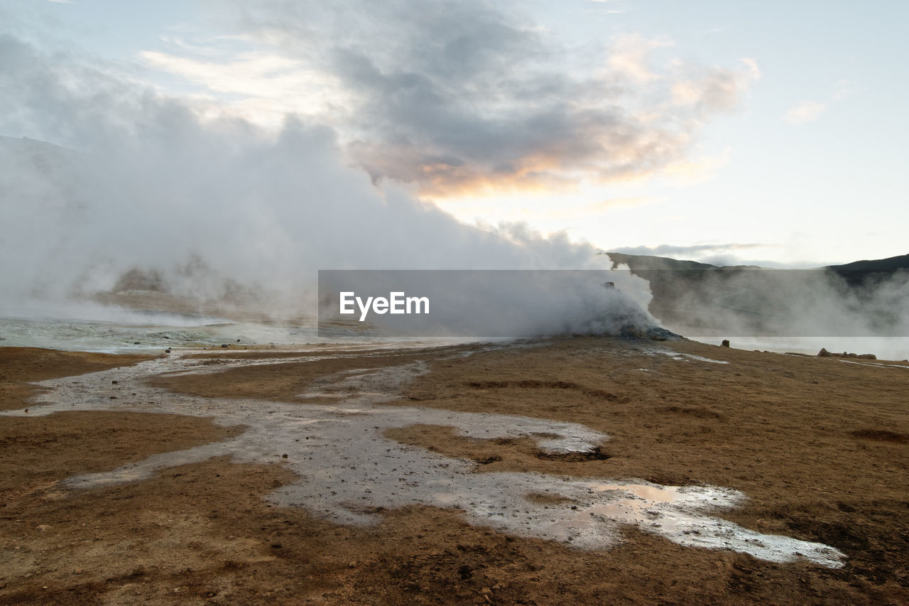 Wide volcanic landscape with a water surface and a lot of steam, which is blown sideways by the wind