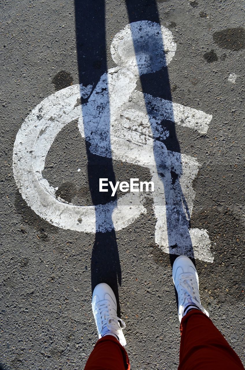 LOW SECTION OF PERSON STANDING ON ROAD SIGN