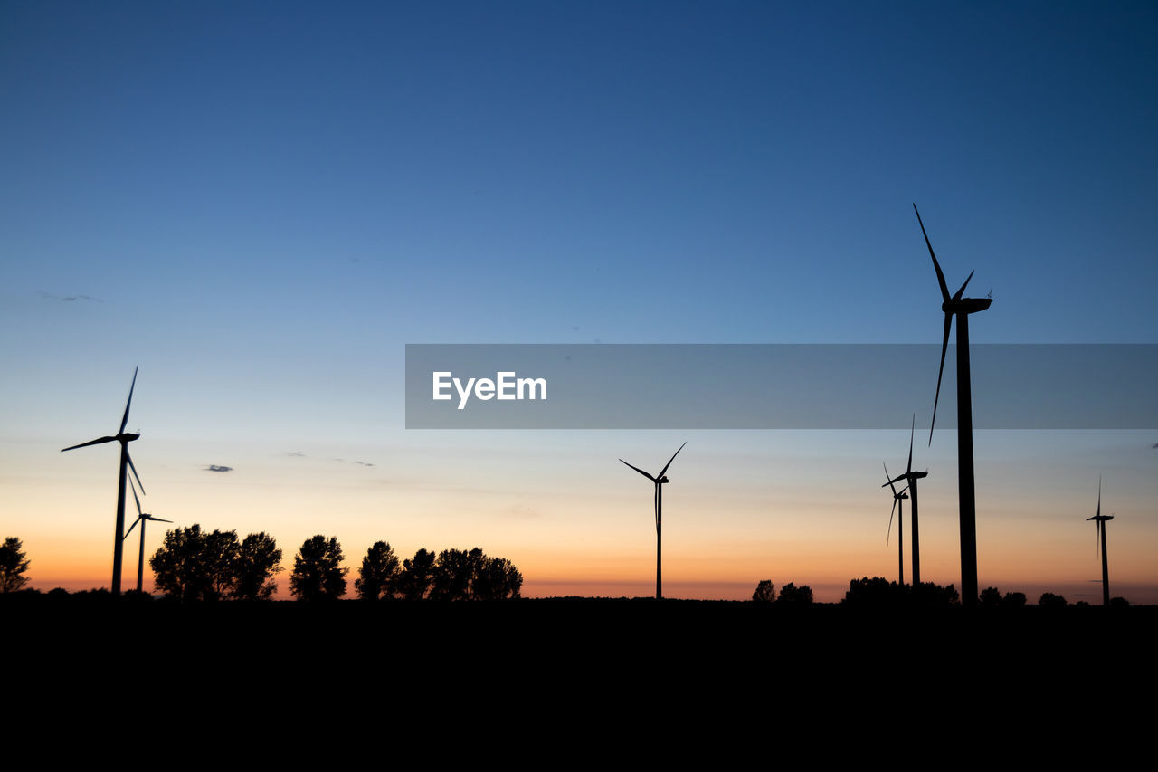 SILHOUETTE WIND TURBINES ON FIELD AGAINST CLEAR SKY