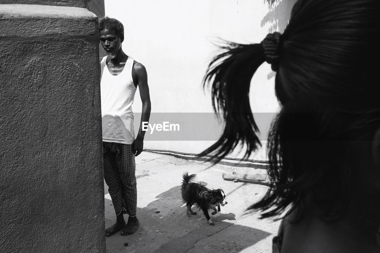 REAR VIEW OF MAN AND WOMAN WITH DOG STANDING ON STREET