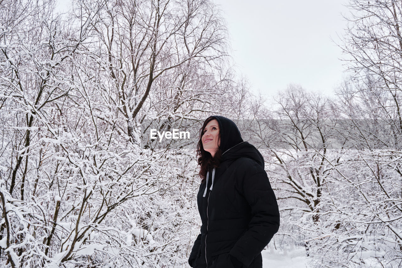 A woman walks alone in a snow-covered park among trees