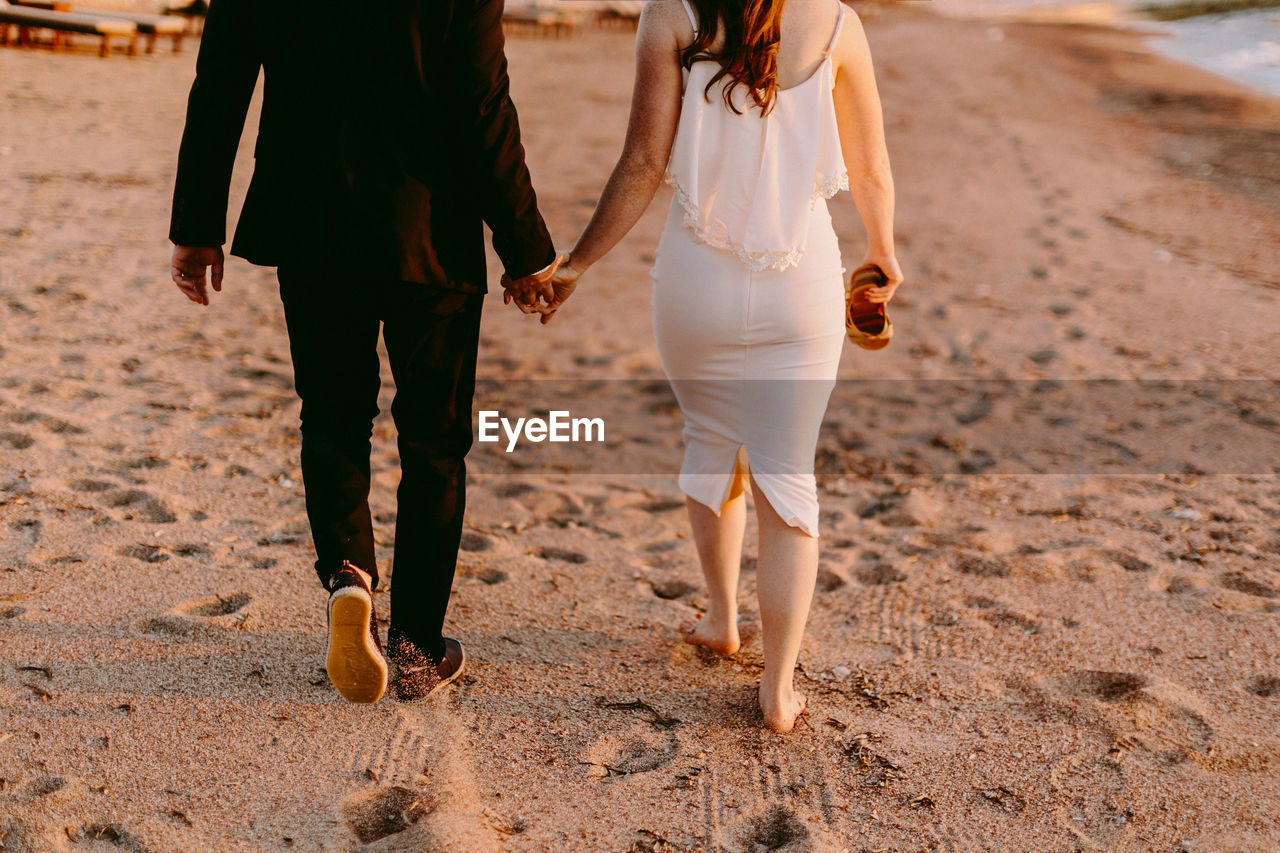 Low section of couple walking at beach