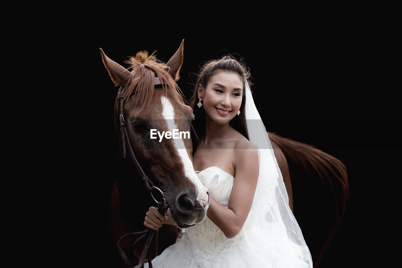 Woman in wedding dress with horse against black background