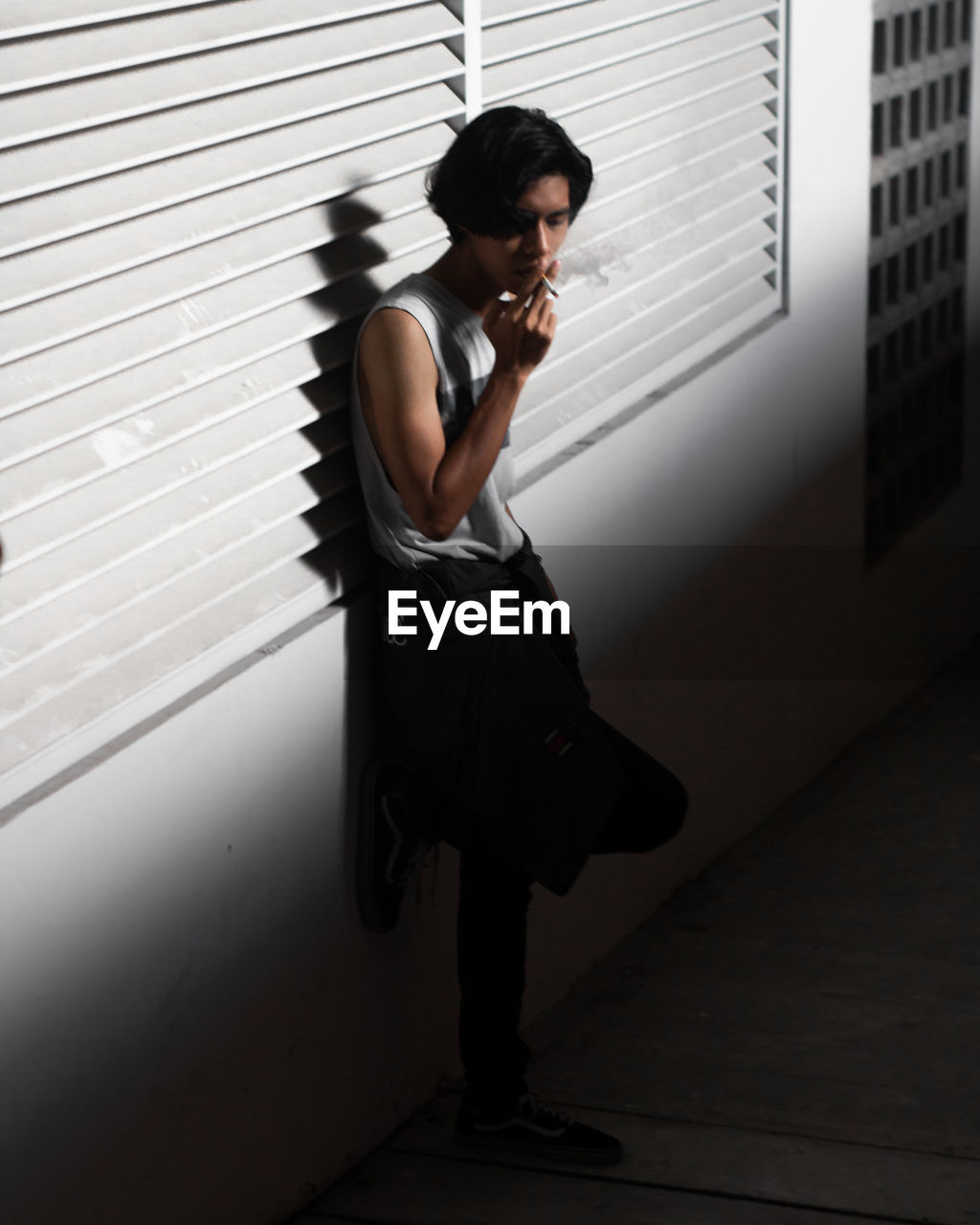 Young man smoking cigarette while leaning on wall