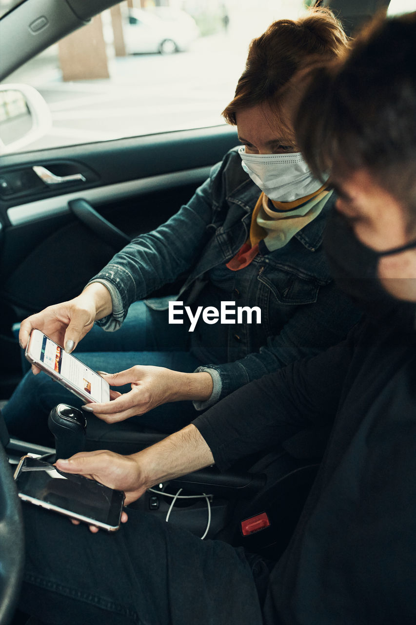 Woman wearing mask holding smart phone sitting at car