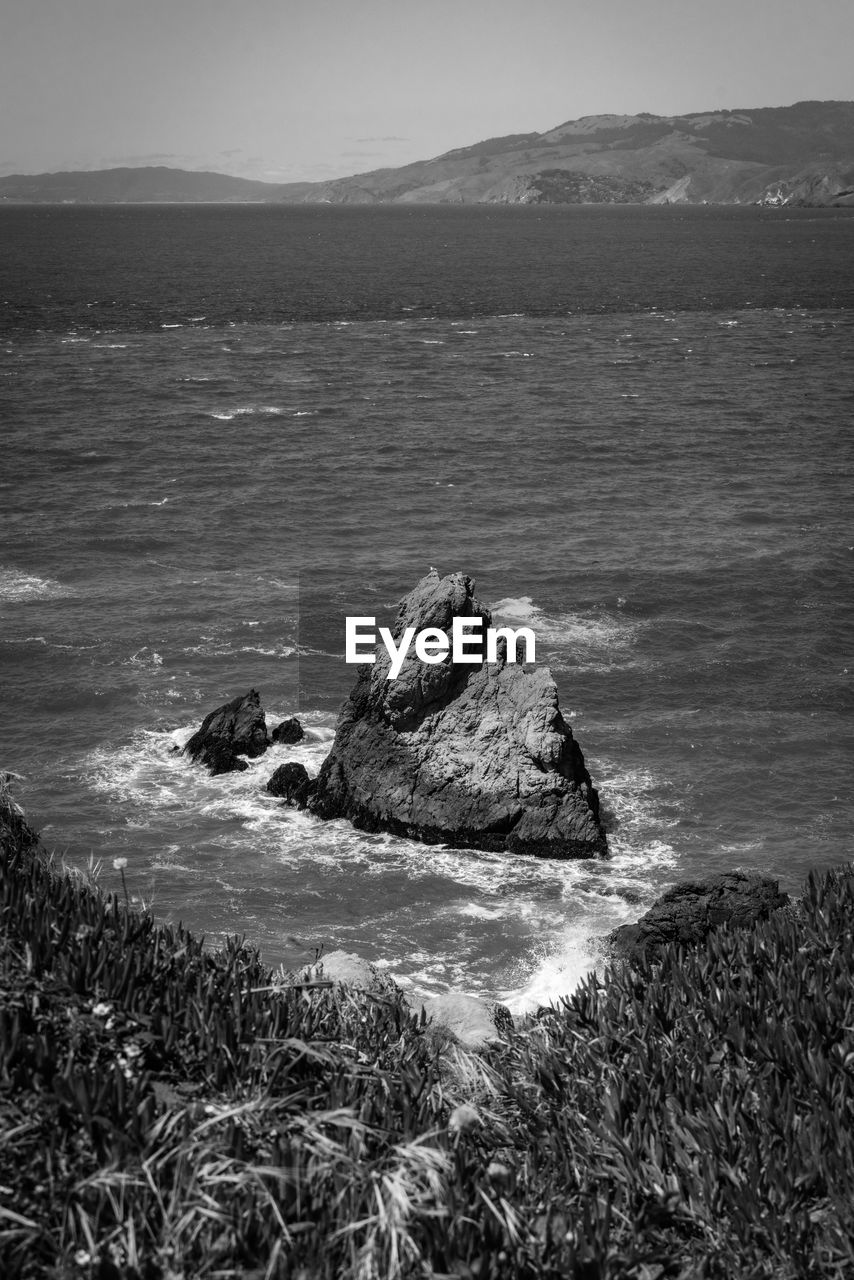 water, rock, sea, black and white, land, monochrome photography, coast, monochrome, scenics - nature, beach, nature, beauty in nature, ocean, shore, sky, tranquility, horizon, wave, no people, environment, tranquil scene, mountain, day, outdoors, landscape, non-urban scene, travel destinations, coastline, body of water, travel, black, plant, remote