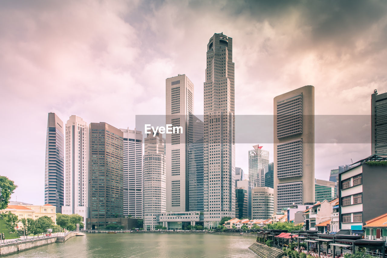 Modern buildings by river against sky in city
