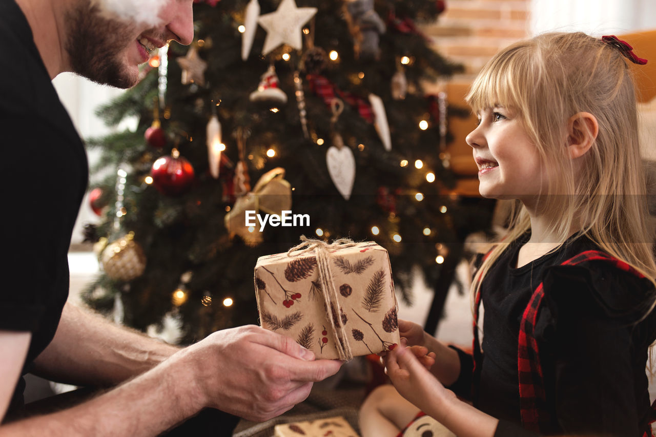 Father gives new year or christmas gift or present to his smiling happy daughter