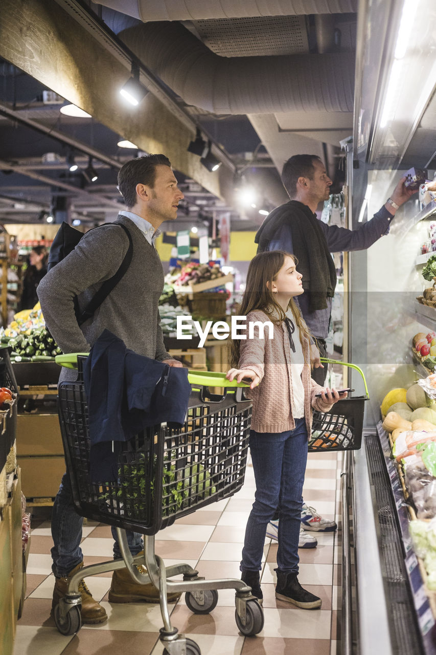 Father and daughter looking for fresh vegetables on shelves in grocery store